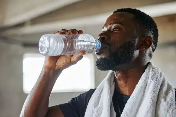 Image of man drinking water to improve hydration Weybridge after work out.